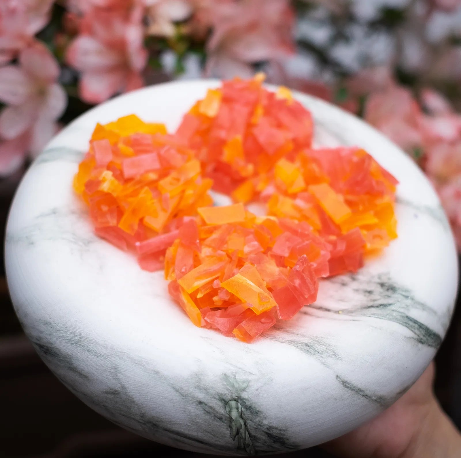 Orange and pink crystal candy clusters on marble; strawberry + orange pairing; thin-cut candy with bright citrus snap.