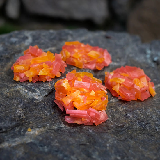 Orange and pink thin-slice crystal candy clusters on dark rock; strawberry + orange flavours; glossy, crunchy yet easy bite.