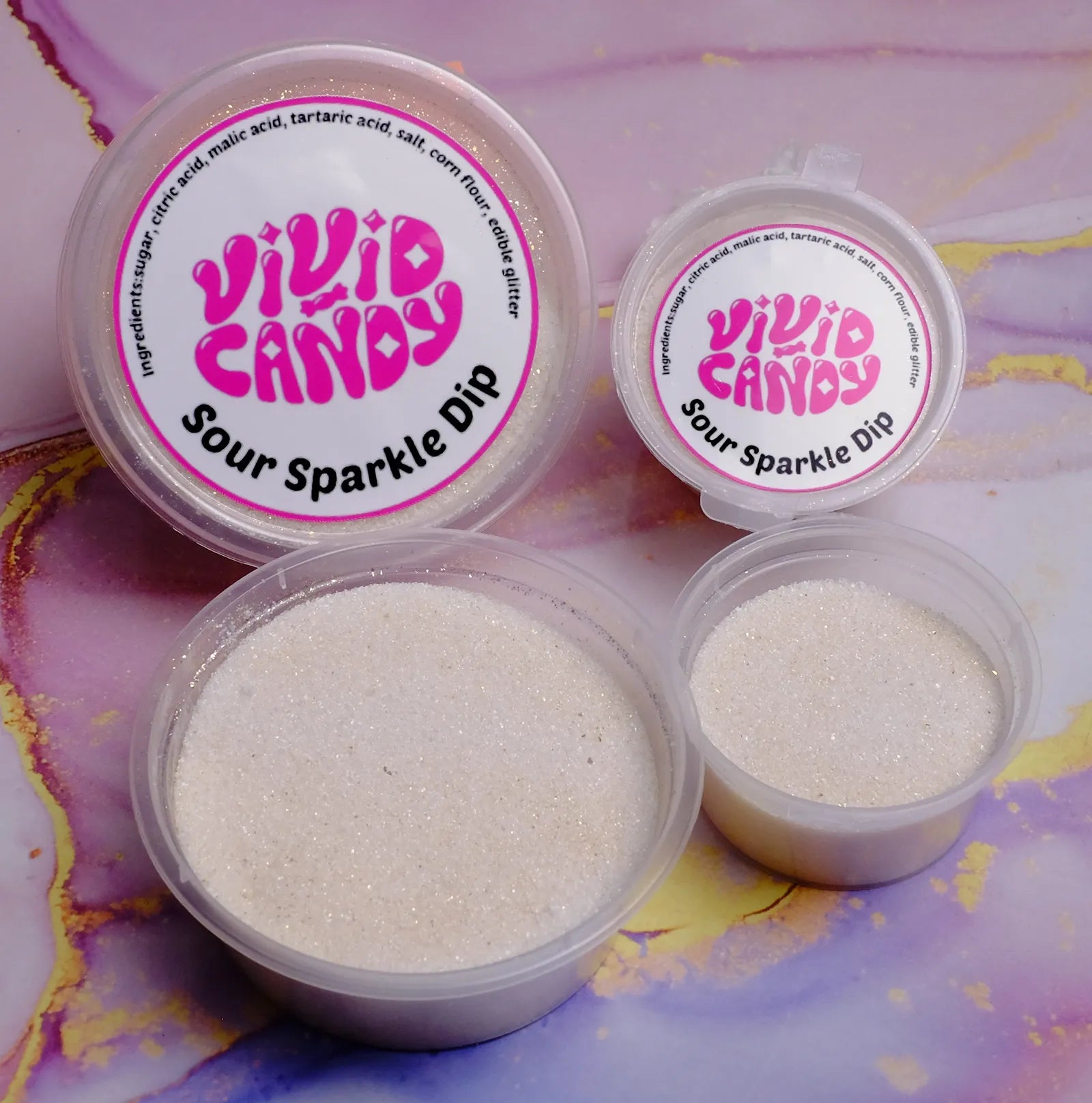 Open and lidded tubs of Sour Sparkle Dip—sparkling sour sugar for crystal candy—on a pastel marble background.