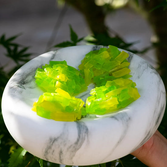 Lime-green and yellow crystal candy clusters arranged on a marble plate in front of maple tree, thin-slice design for clean crunch.