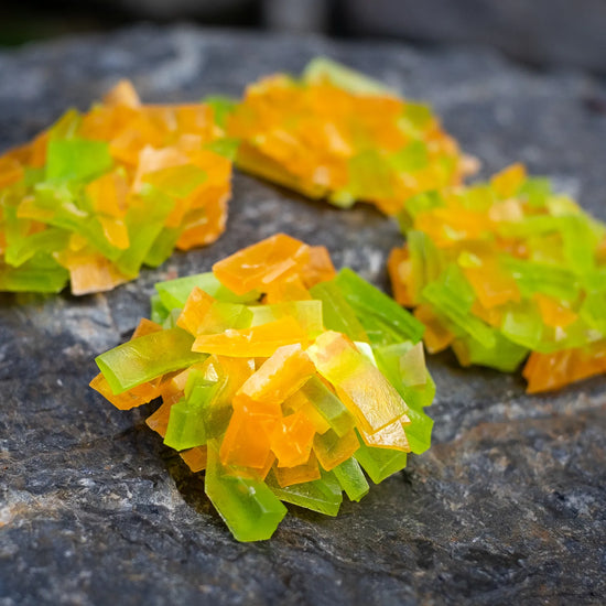Green and orange crystal candy clusters slices on dark stone; lime + orange citrus pairing, glossy crunchy shards.