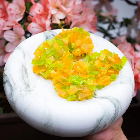 Lime-green and orange crystal candy clusters on a white marble plate; citrus duo in thin-cut shards, bright and crunchy.