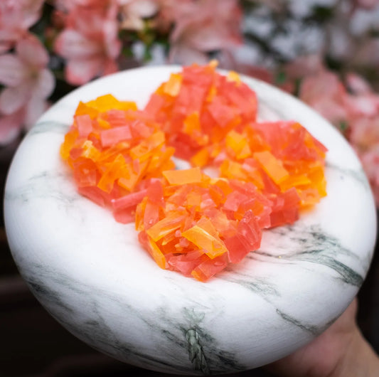 Orange and pink crystal candy clusters on marble; strawberry + orange pairing; thin-cut candy with bright citrus snap.