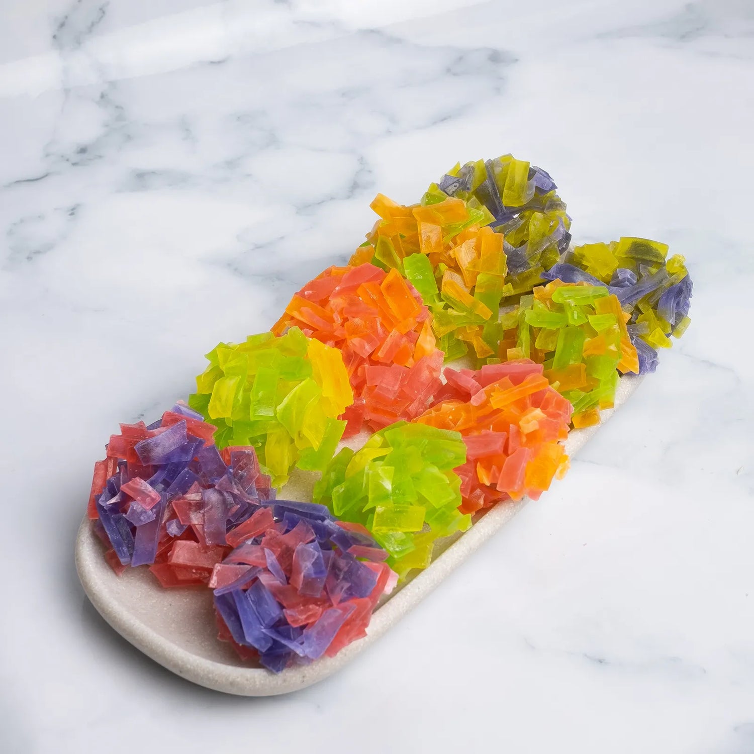 Long stone platter filled with jewel-bright thin-slice crystal candy clusters in purple, green, orange and red. Thin-slice shards with ASMR crunch.
