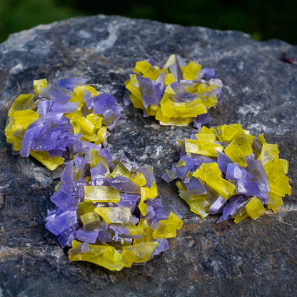 Purple and yellow thin-slice crystal candy clusters (pineapple + blueberry) clustered on dark rock; glossy shards with crunchy snap.