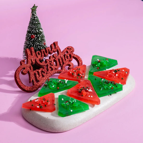 Decorative Christmas crystal candy with red and green crystal candy, 'Merry Christmas' sign, and small Christmas tree on a pink background.