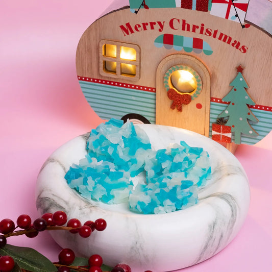 A Christmas blue and white crystal candy clusters with a small wooden house, blue crystal-like object, and red berries on a pink background.